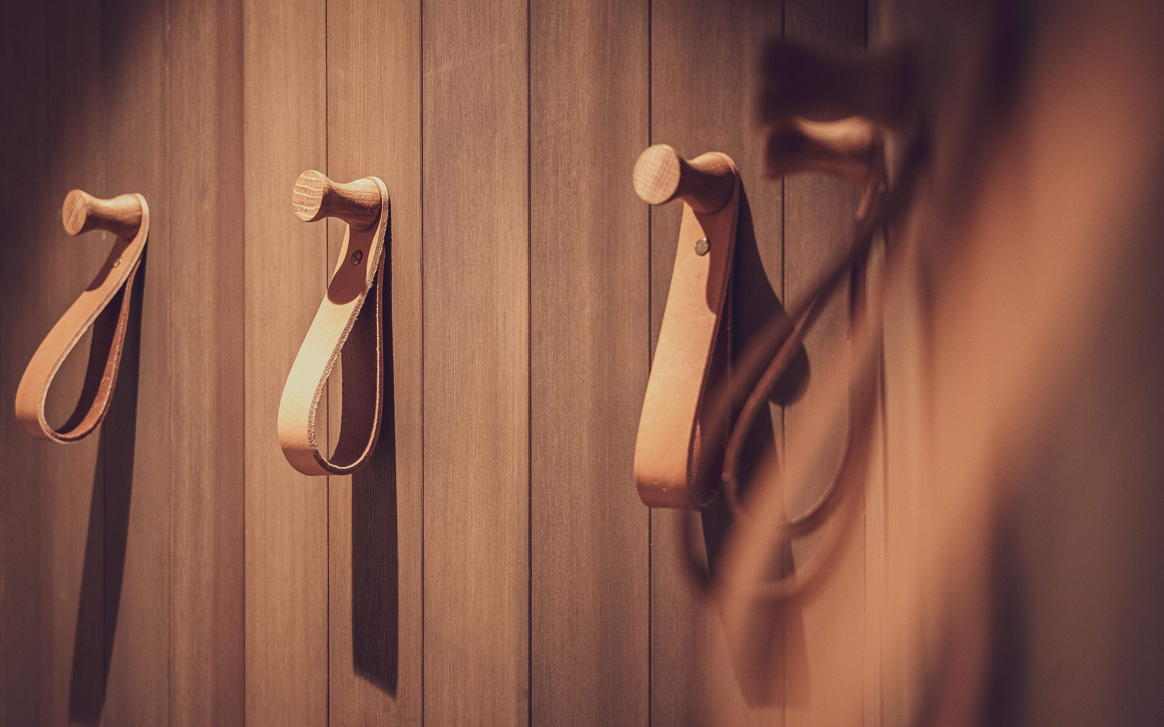 A wooden wall with three leather straps hanging.