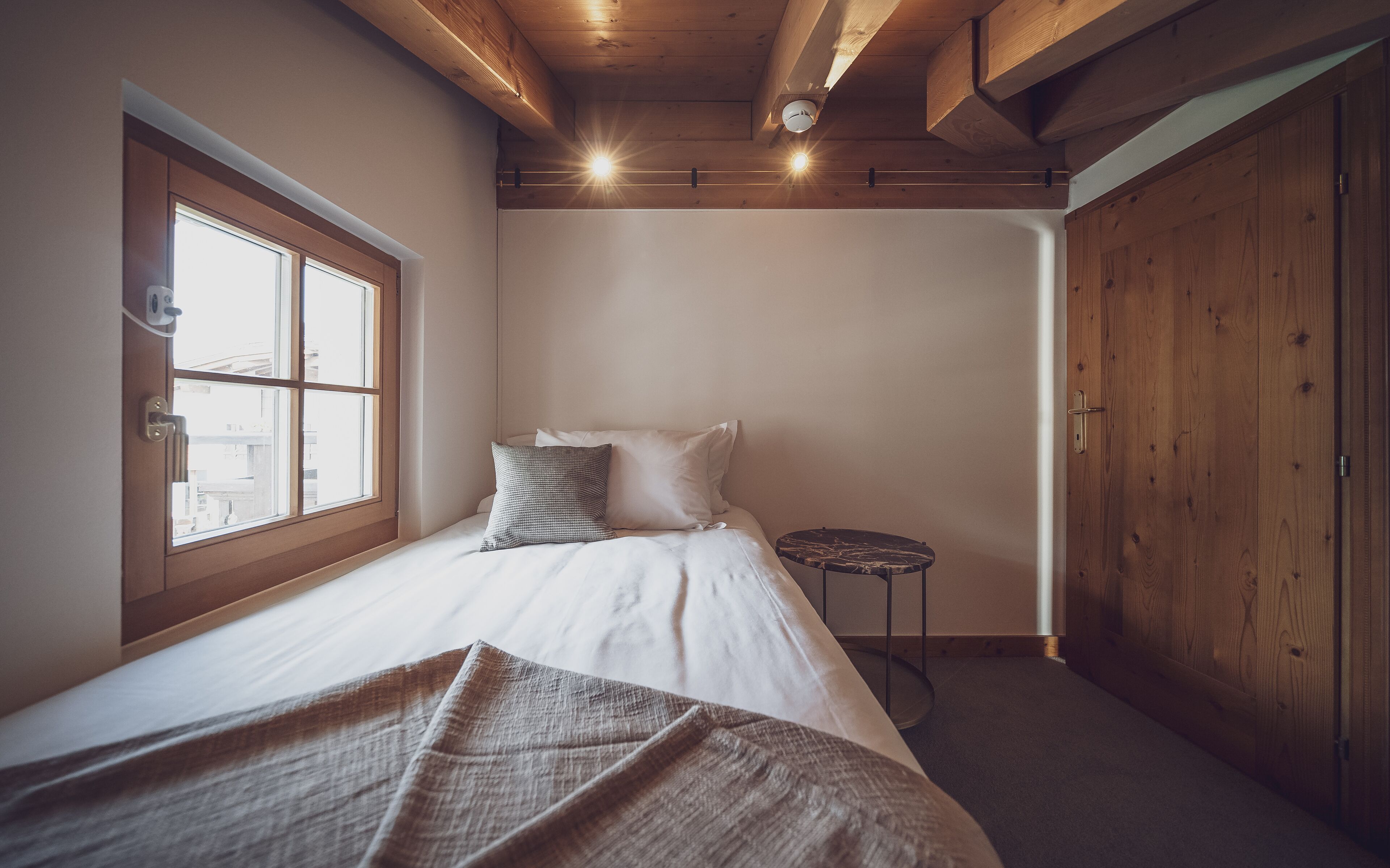 A bedroom with a bed, a window, a small round table, and a wardrobe.