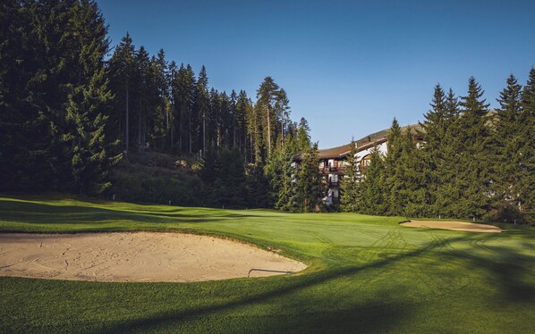 A golf course with sand bunkers, a clubhouse, and surrounding tall trees. - Hotel Waldhuus Davos (Davos)