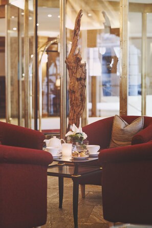 A cozy seating area with a wooden coffee table, red upholstered chairs, and a vase of flowers. - Hotel Waldhuus Davos (Davos)
