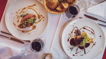 Una mesa de comedor con platos de comida, una cesta de pan y vasos de una bebida oscura.
