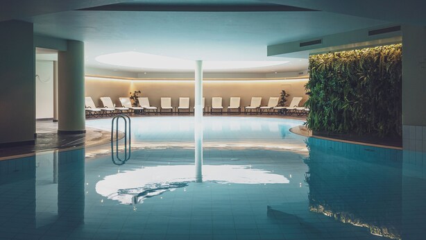 An indoor swimming pool with lounge chairs and a green wall. - Hotel Waldhuus Davos (Davos)