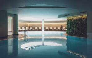 An indoor swimming pool with lounge chairs and a green wall. - Hotel Waldhuus Davos (Davos)