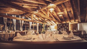 A restaurant with wooden beams, round tables set for dining, and a warm interior ambiance. - Hotel Waldhuus Davos (Davos)