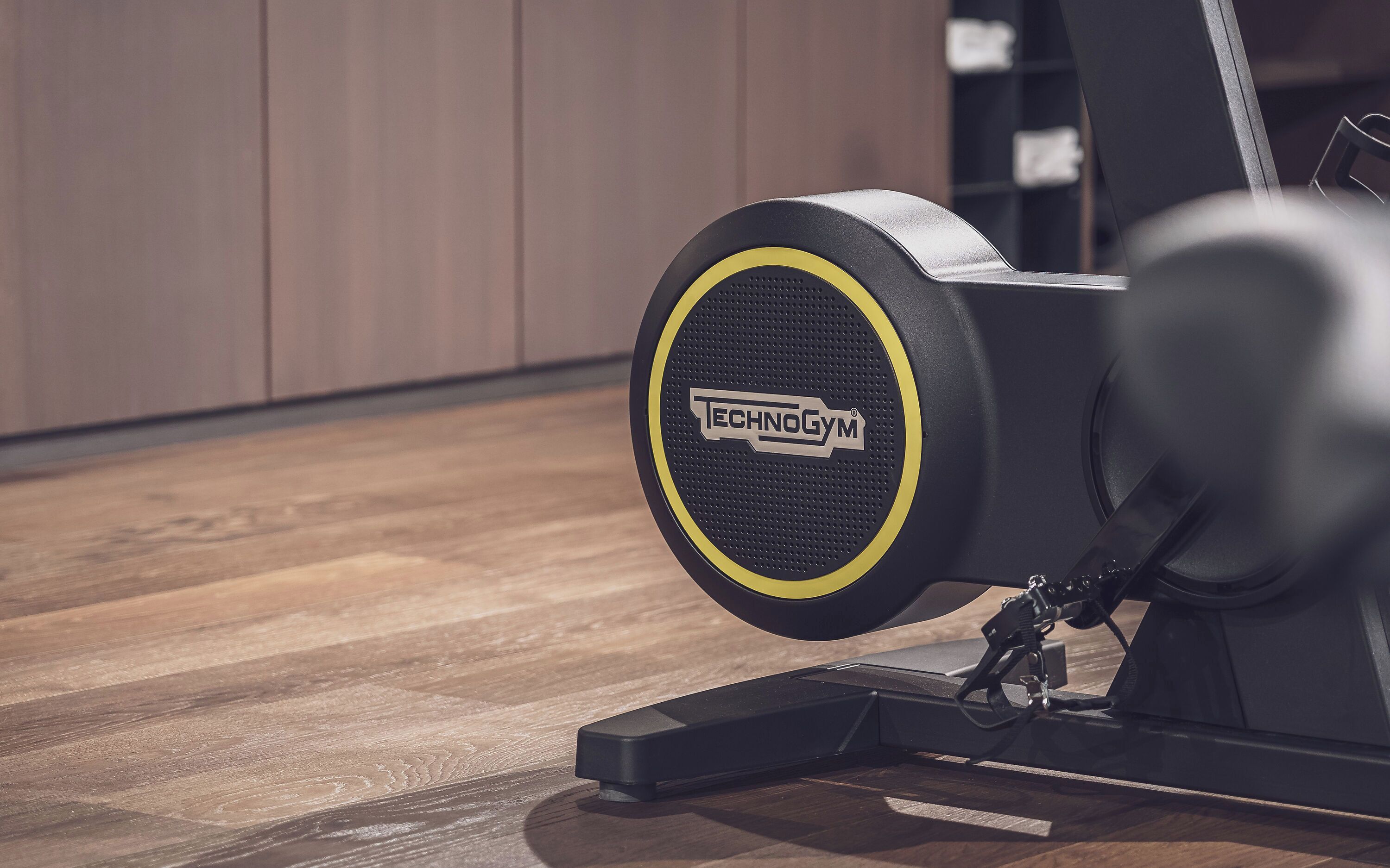 A stationary exercise bike with a visible brand logo, a control panel, and a wooden floor.
