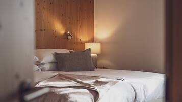 Ein ordentlich bezogenes Bett mit weißen Leinen und einer braunen Tagesdecke, ein hölzernes Kopfende, eine Nachttischlampe und eine Wandleuchte.