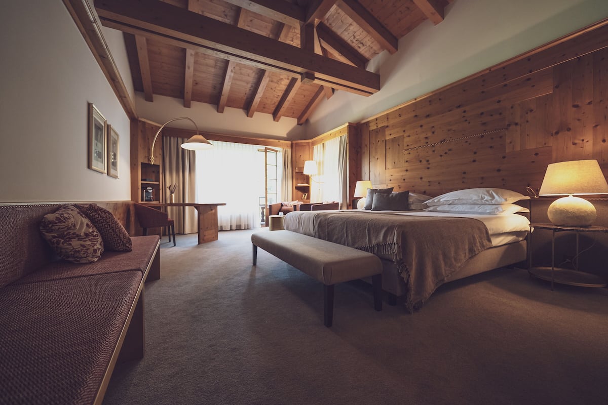 A cozy bedroom with a large bed, a bench, a desk, and a lamp.