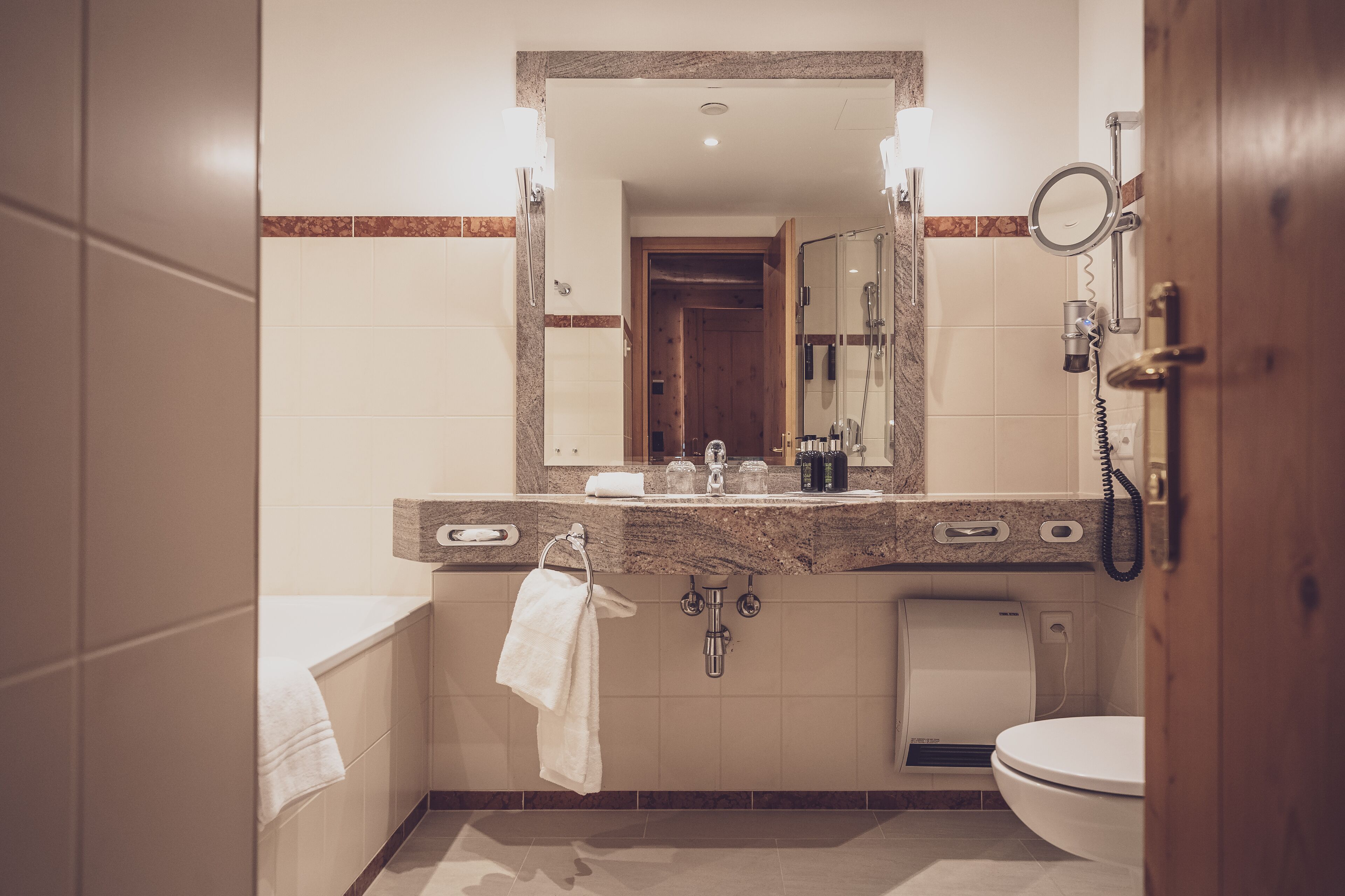 A modern bathroom with a marble sink, a large mirror, a handheld showerhead, and a toilet.