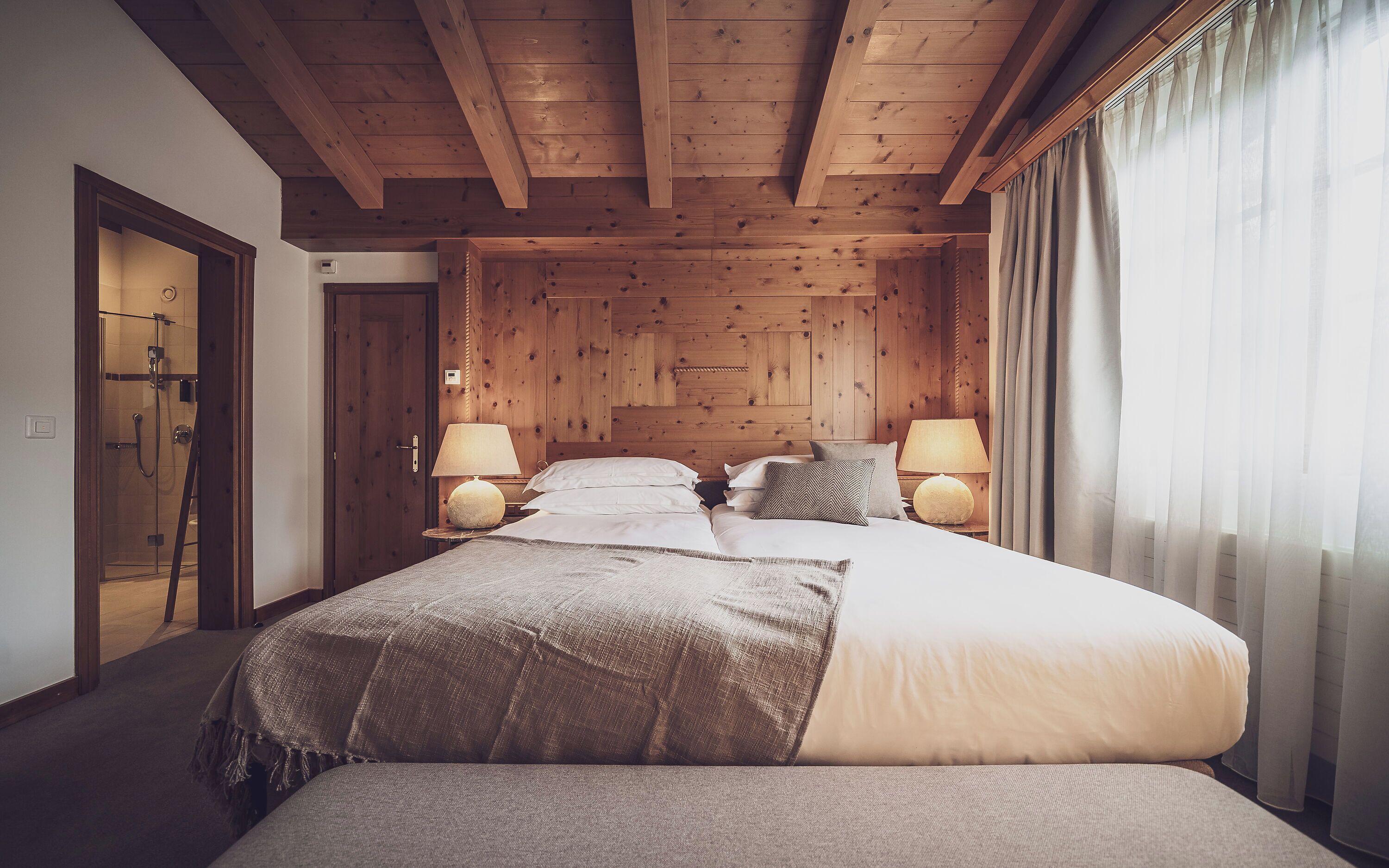 A wooden-paneled bedroom with a bed, two bedside lamps, and a shower door.