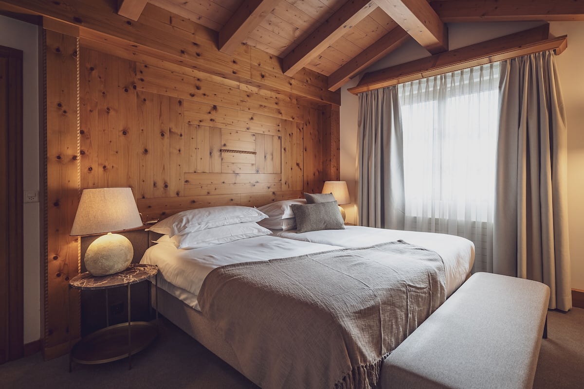 A wooden-paneled bedroom with a bed, two bedside lamps, and a window with curtains.