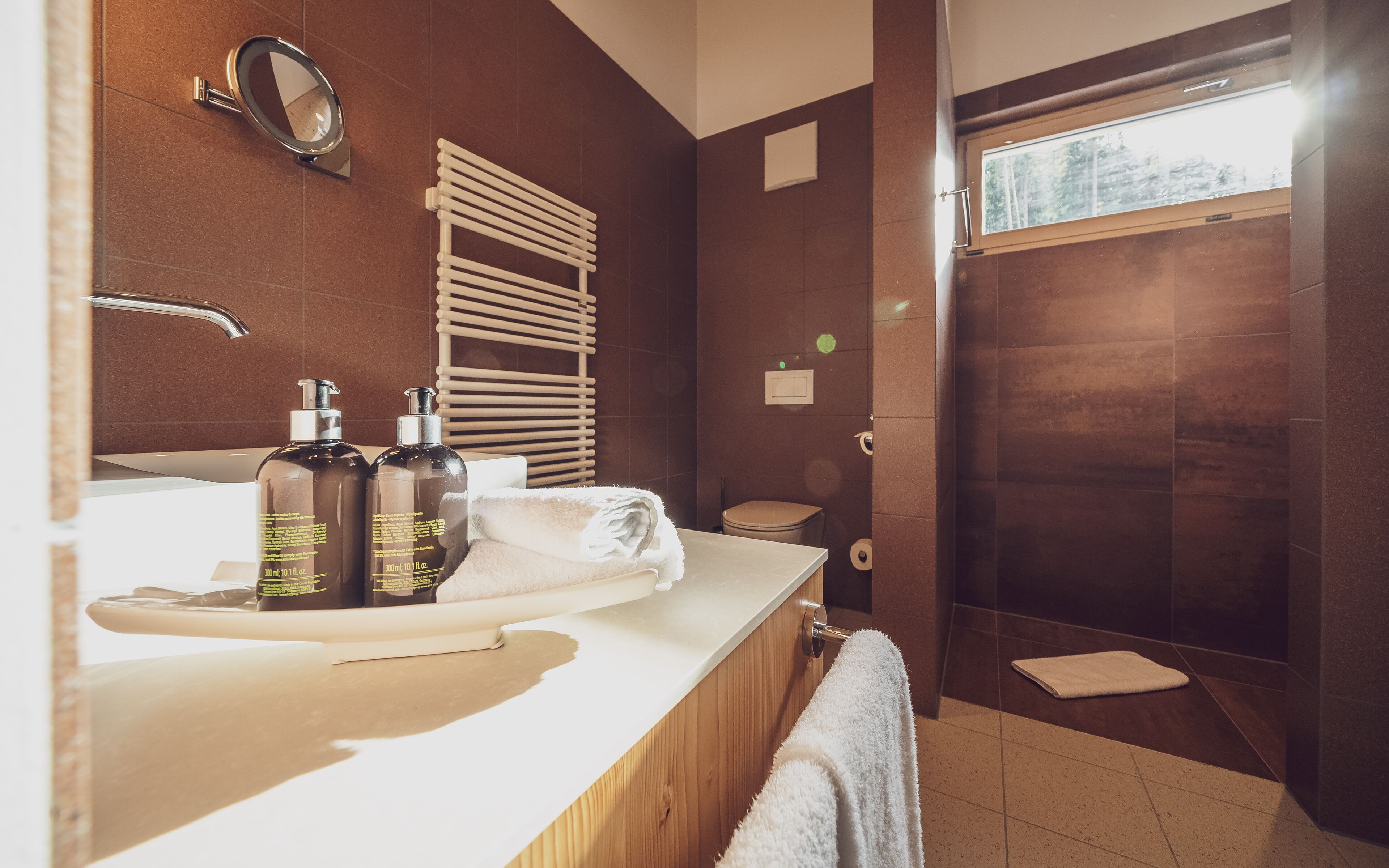 Un baño moderno con un tocador de madera, un espejo, dos botellas de champú, una toalla y una zona de ducha.