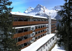 A multi-story hotel with balconies, surrounded by snow-covered mountains and trees. - Sunstar Hotel Arosa (Arosa)