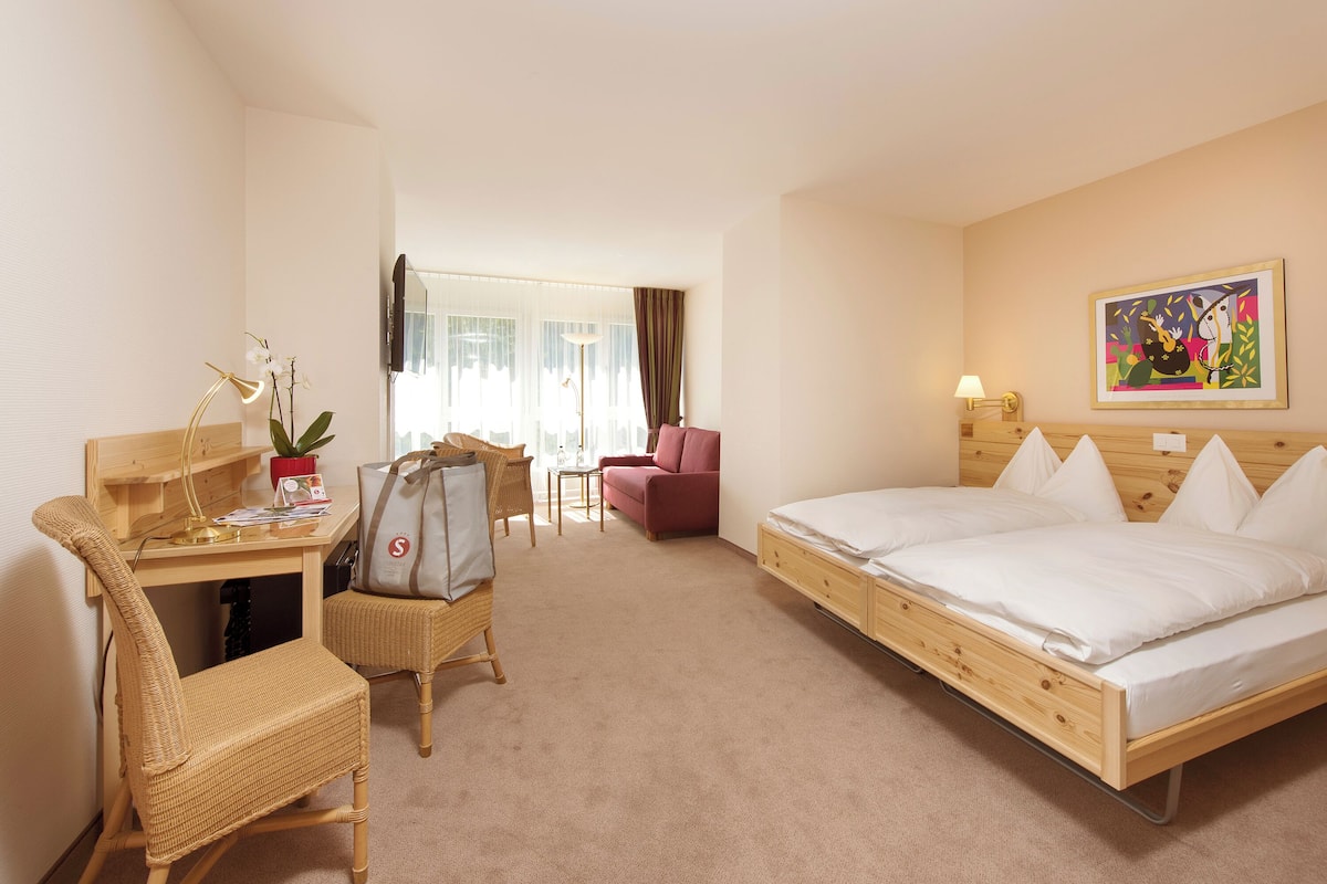 A hotel room with a bed, desk, chair, and a painting on the wall.