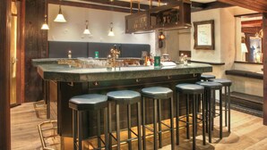 A bar area with a wooden ceiling, bar stools, and hanging pendant lights. - Sunstar Hotel Arosa (Arosa)