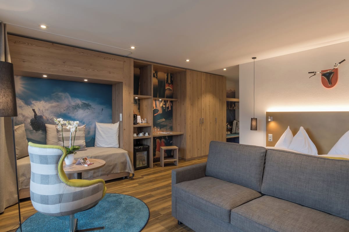 A modern room with a bed, a grey sofa, a striped chair, a small table, and a blue rug.