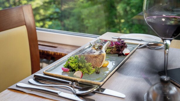A table set with a meal, a wine glass, and a view of a forest and mountains. - Sunstar Hotel Arosa (Arosa)