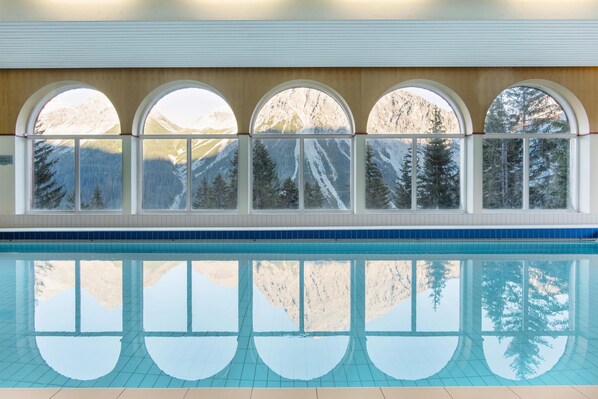 A swimming pool with a view of mountains through arched windows. - Sunstar Hotel Arosa (Arosa)