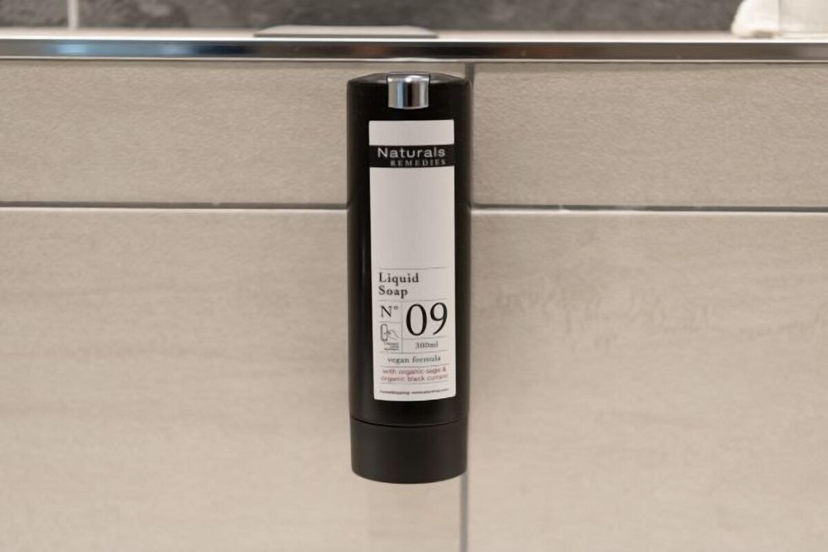 A black bottle of Naturals Remedies Liquid Soap with a white label, hanging on a beige tiled wall.