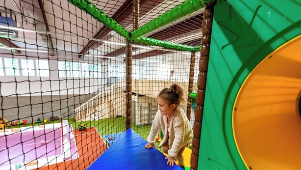 A child playing in a play area with a netted enclosure, a blue mat, and colorful play structures. - Sunstar Hotel Arosa (Arosa)