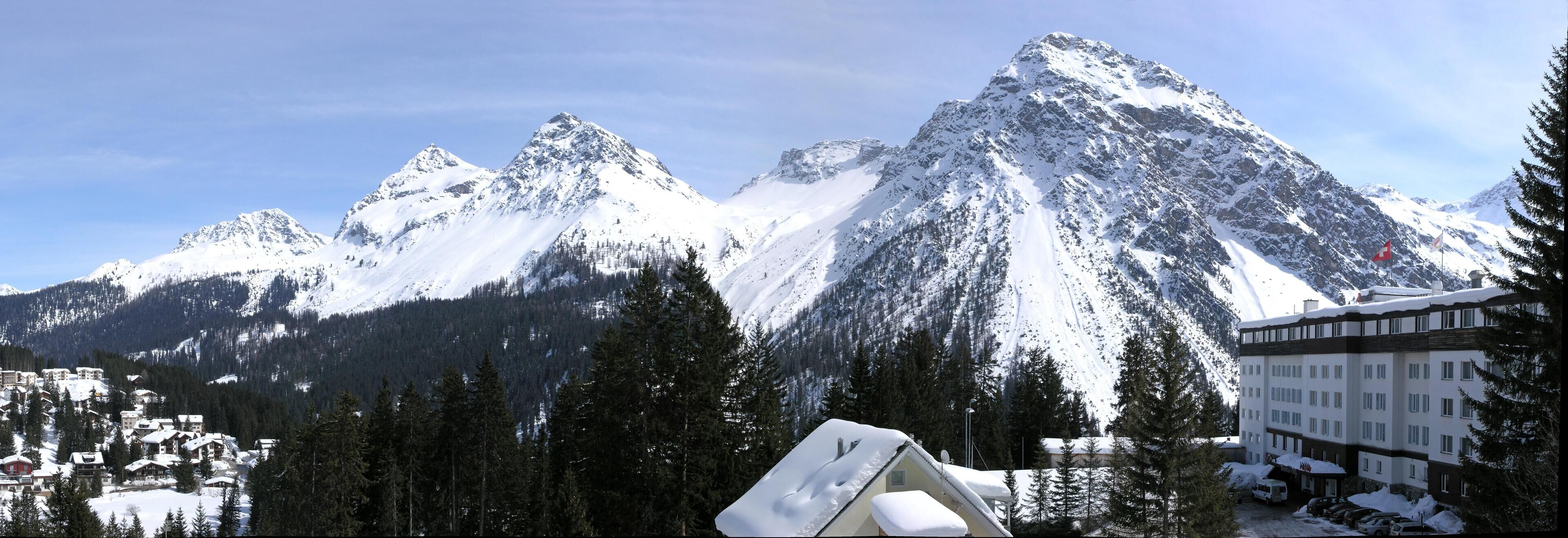 Une station de montagne avec des sommets enneigés, un chalet à étages et un parking.