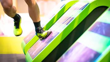 Une personne court sur un tapis de course vert et incurvé, avec un fond rayé de violet et de blanc.