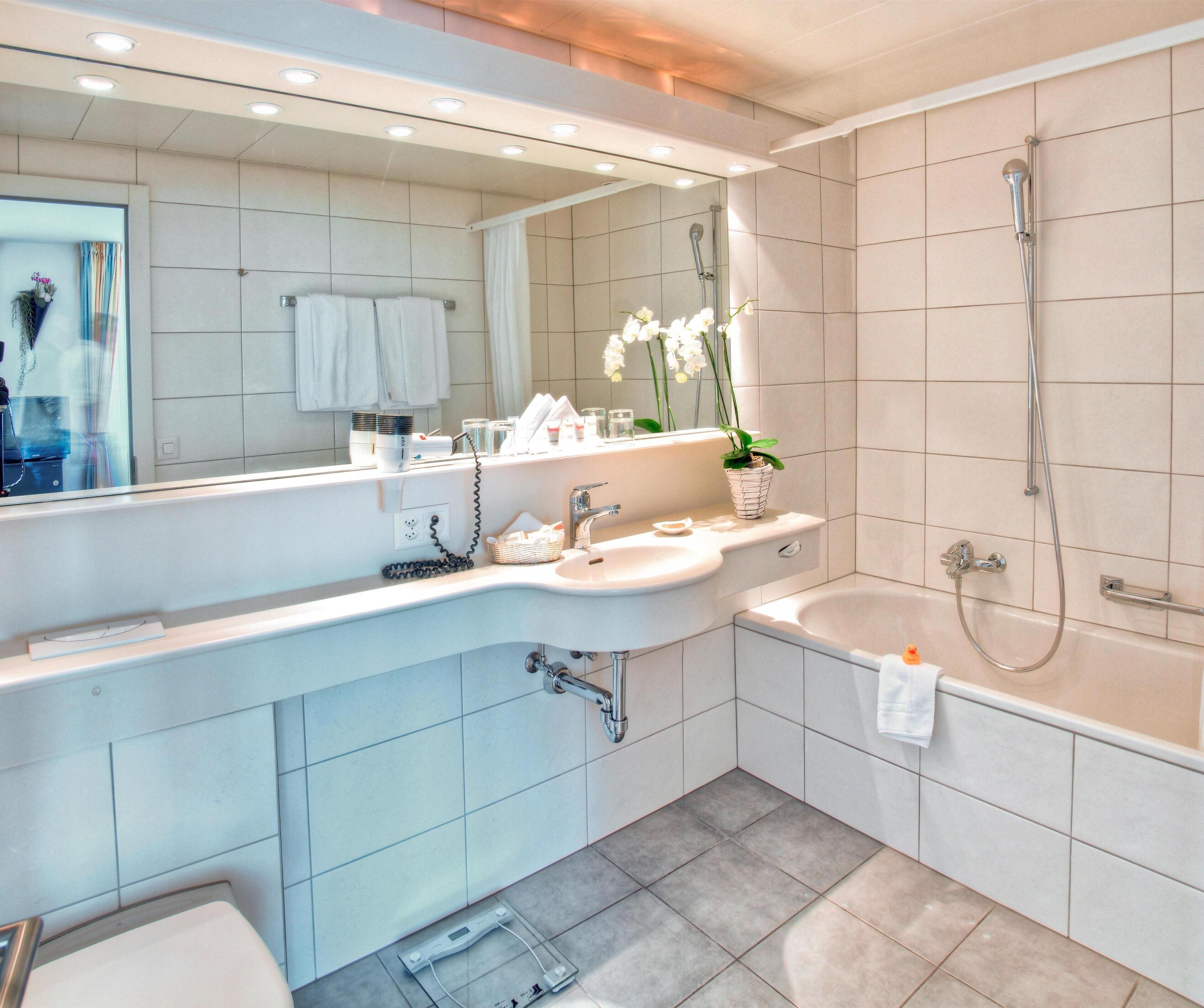 A modern bathroom with a large mirror, a sink, a bathtub, and a shower.