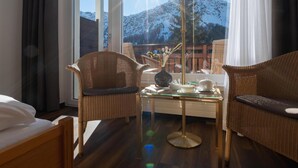 A hotel room with a bed, two wicker chairs, a glass coffee table, and a view of snow-capped mountains. - Sunstar Hotel Arosa (Arosa)