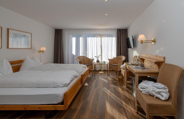 Habitación de hotel con una cama grande, un escritorio con silla, televisor y ventana con cortinas.