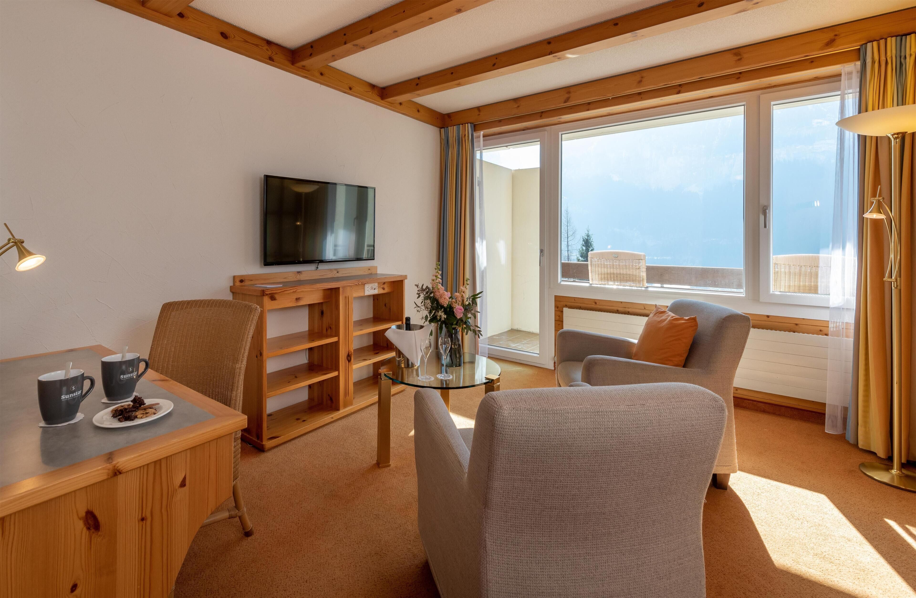 A cozy living room with a wooden ceiling, a flat-screen TV, a glass coffee table, a sofa, and a dining table with chairs.