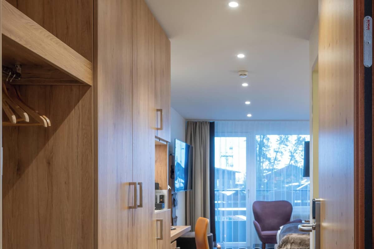 Une chambre d’hôtel avec une armoire en bois, un bureau avec une chaise, un lit avec une couverture et un téléviseur.