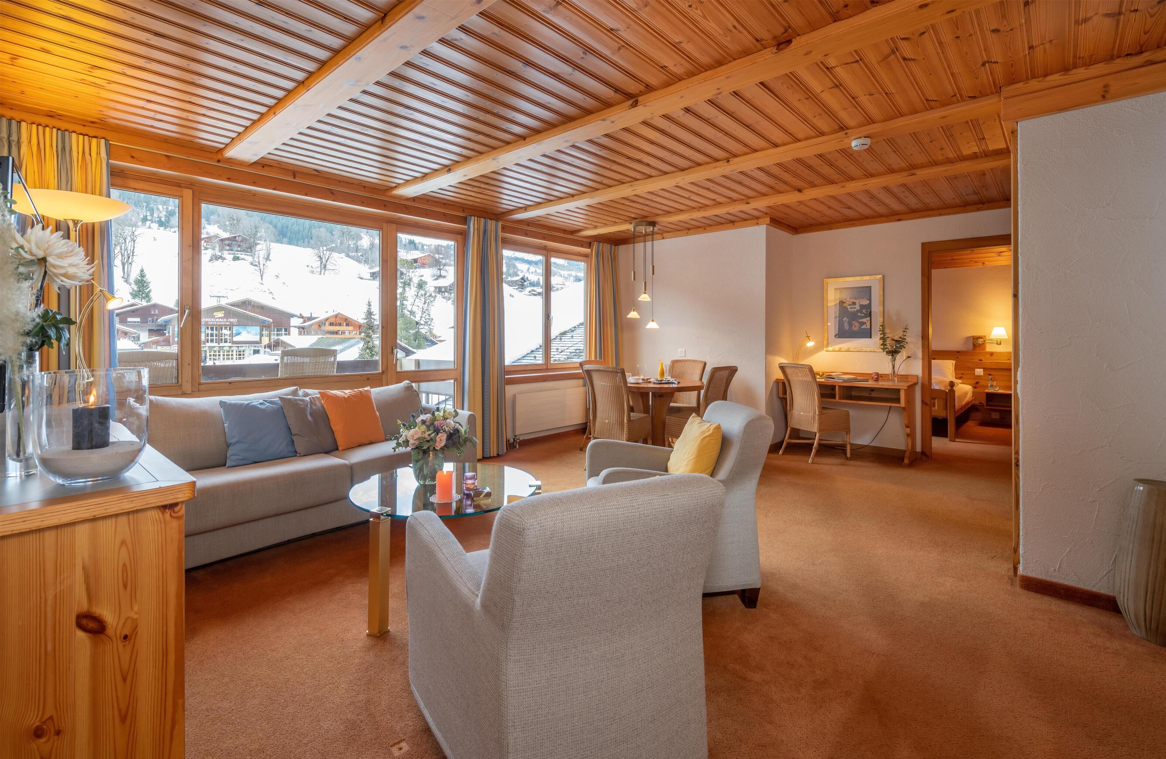 Un salon chaleureux avec un plafond en bois, de grandes fenêtres, un canapé, une table à manger et un fauteuil.