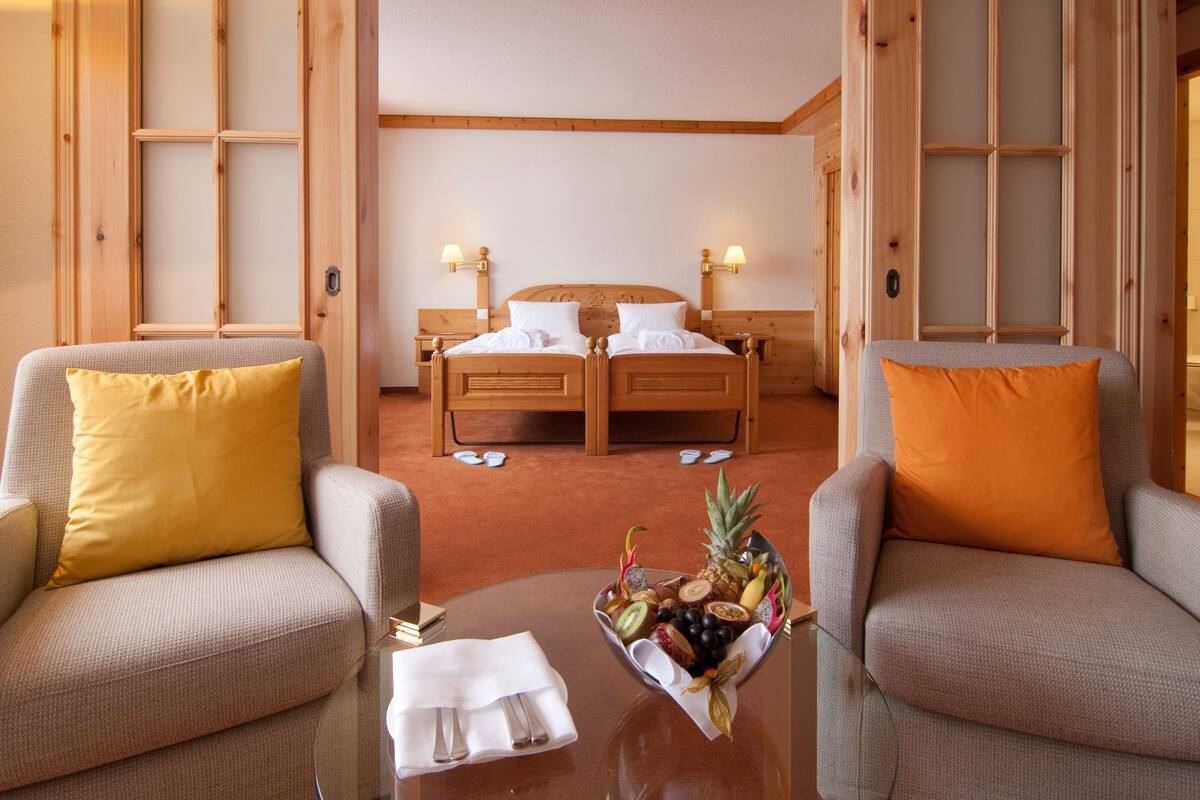 Une chambre d’hôtel comprenant un lit, deux fauteuils, une table basse et un panier de fruits.