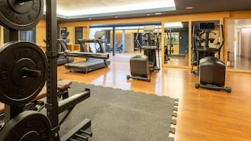 Ein Fitnessstudio mit unterschiedlichen Trainingsgeräten, darunter Laufbänder und Kraftgeräte, sowie einem Holzboden.