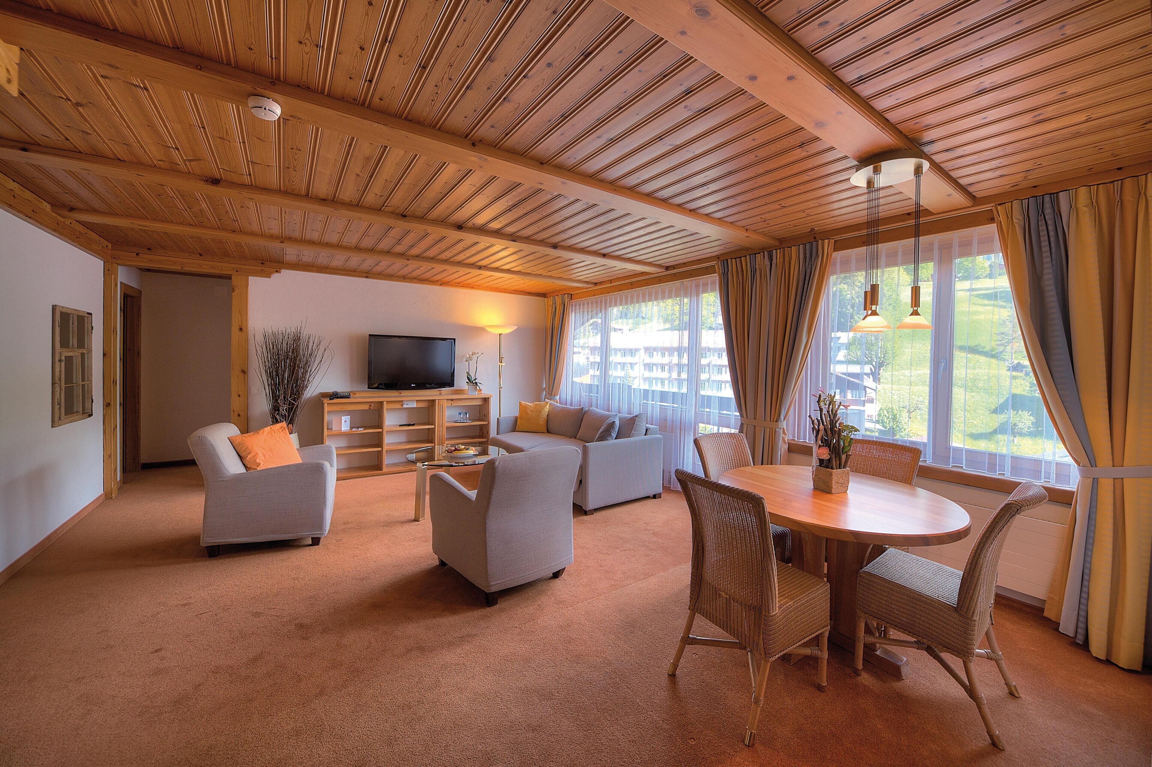 Una sala de estar acogedora con techo de madera, un conjunto de sofás, un televisor y un comedor con sillas de mimbre.