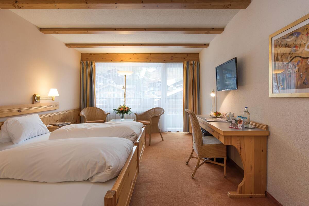 Une chambre d’hôtel avec deux lits, un bureau, une chaise, une télévision et une fenêtre avec des rideaux.