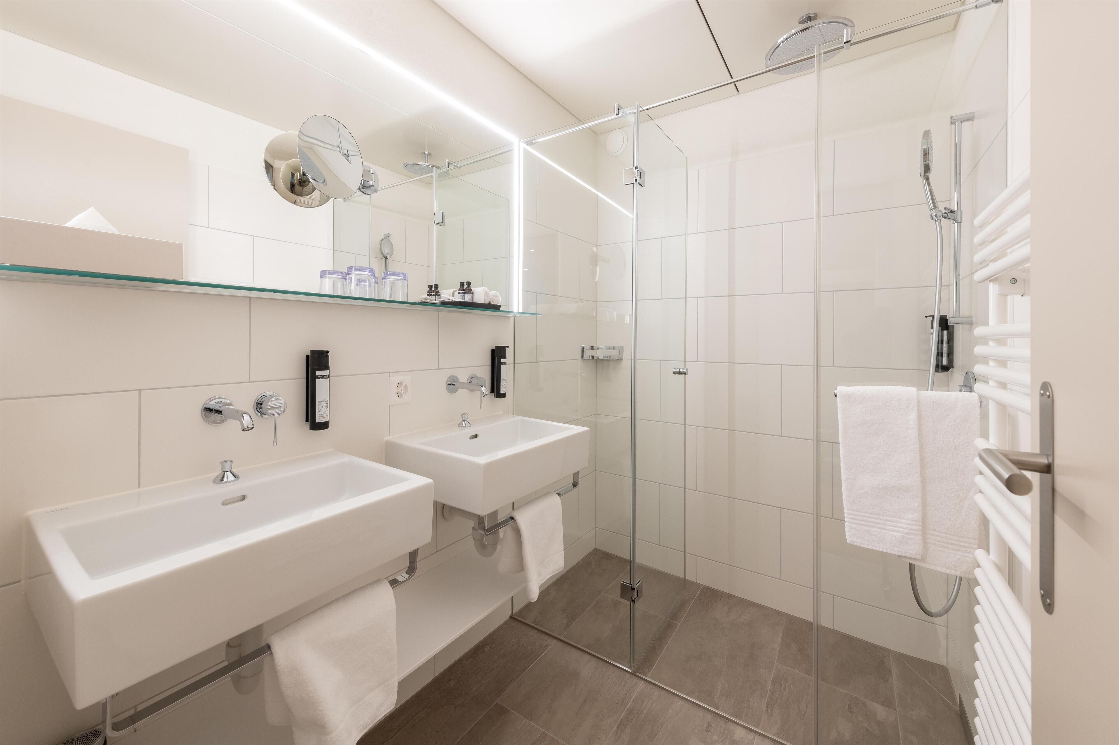 A modern bathroom with two sinks, a glass shower enclosure, and a towel rack.