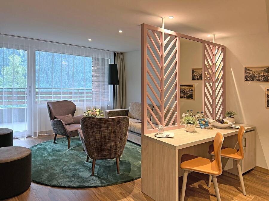 Habitación de hotel moderna con un escritorio de madera, dos sillas, un espejo grande y vistas al exterior a través de amplios ventanales.