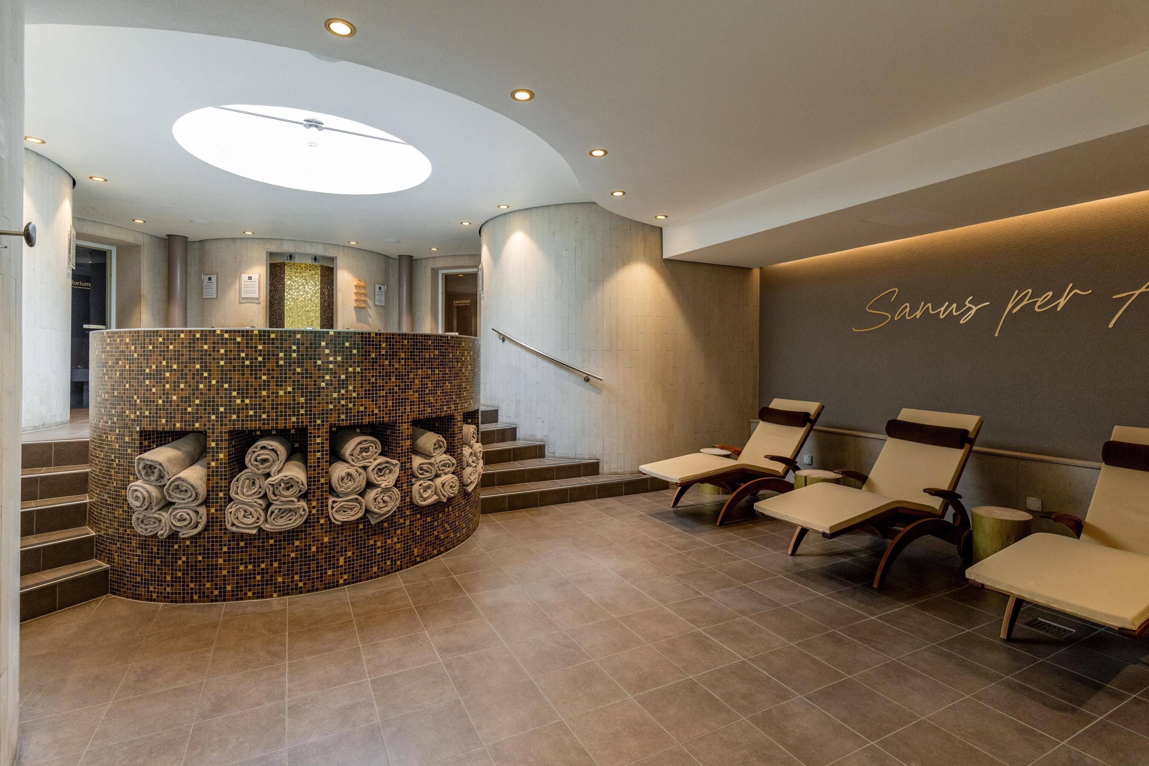 A modern lobby with a curved reception desk, a staircase, and a seating area with chairs.