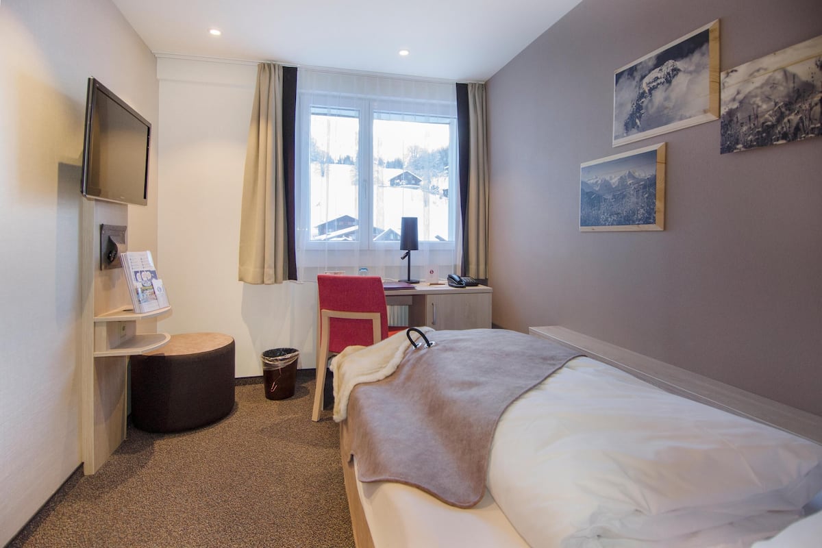 Une chambre d’hôtel équipée d’un lit, d’un bureau, d’une chaise, d’une télévision et d’une fenêtre avec des rideaux.