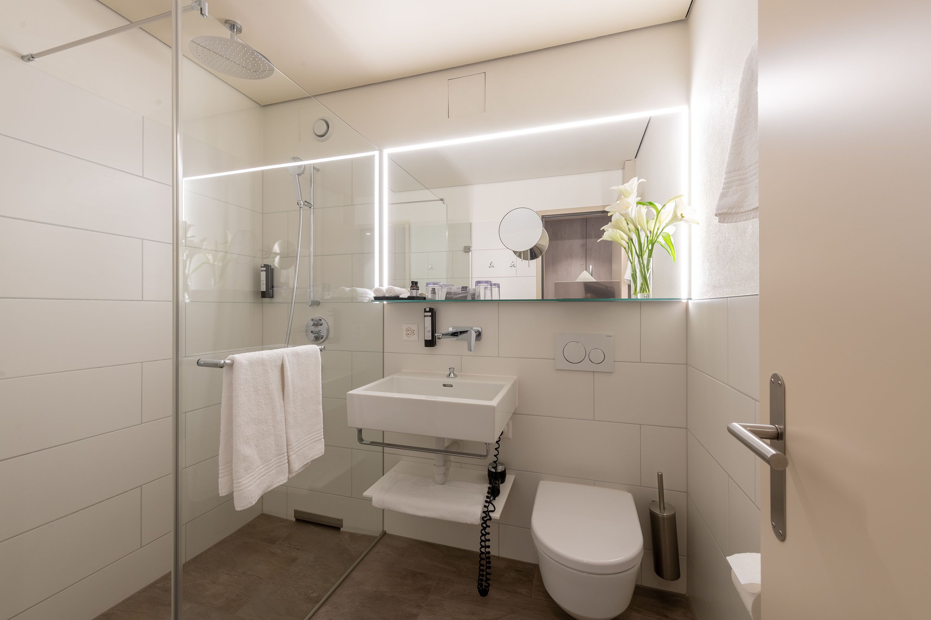 Un baño moderno con cabina de ducha de vidrio, un lavabo blanco, un inodoro y un espejo sobre el lavabo.