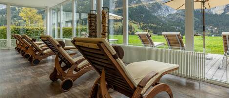 A sun lounge with wooden chairs and a view of mountains.