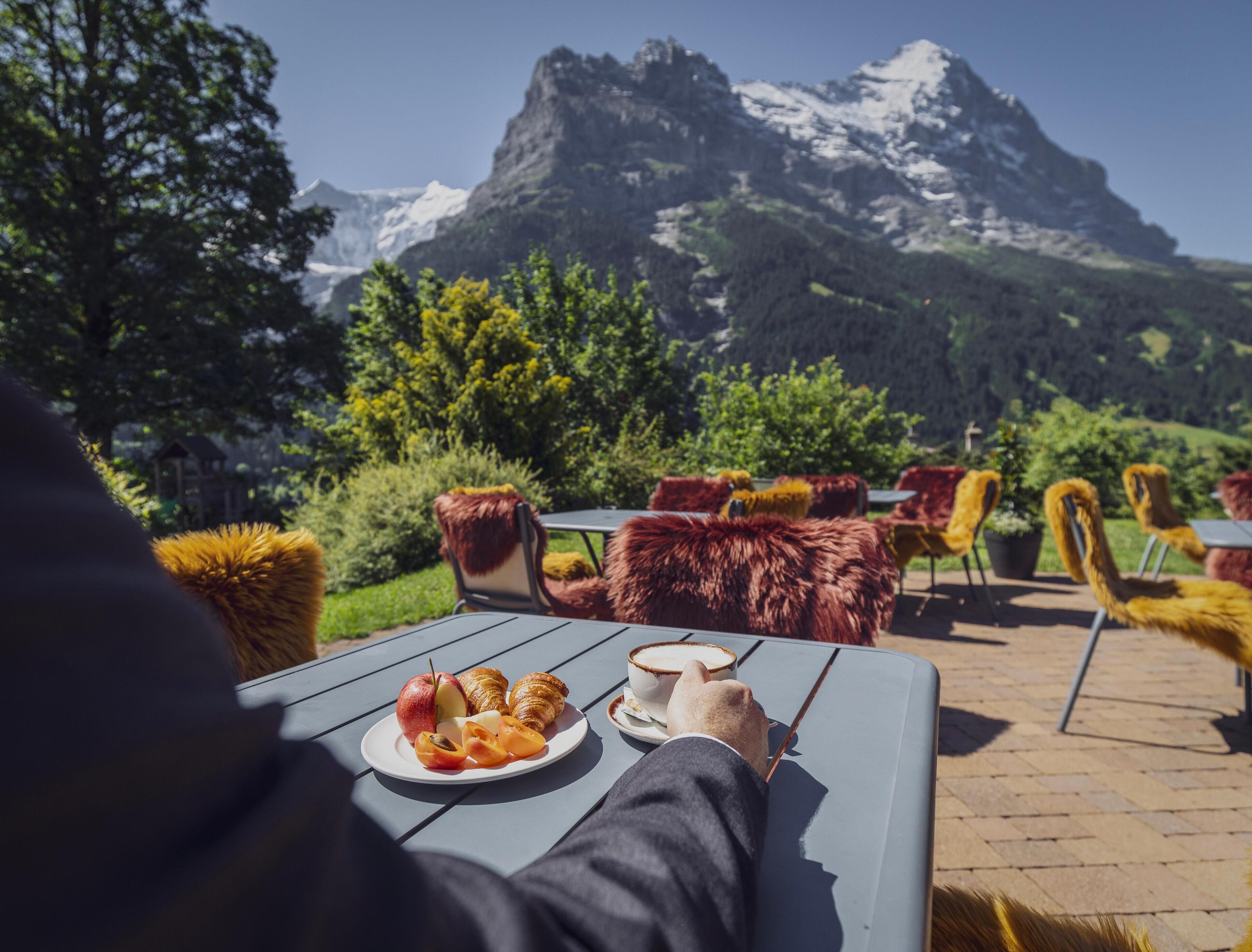 Une table avec une assiette de nourriture et une tasse, installée à l’extérieur, avec une vue sur la montagne.