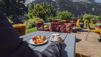 Une table avec une assiette de nourriture et une tasse, installée à l’extérieur, avec une vue sur la montagne.