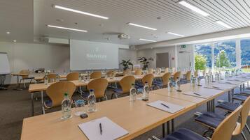 Un salón de conferencias con mesas largas, sillas, botellas de agua y una pantalla de proyector que muestra 'Sunstar'.