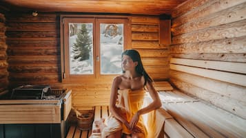 Interior de una cabaña de madera con un banco de sauna, un banco de madera y una ventana que ofrece vistas de un paisaje nevado.