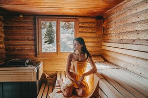 Interior de una cabaña de madera con un banco de sauna, un banco de madera y una ventana que ofrece vistas de un paisaje nevado.