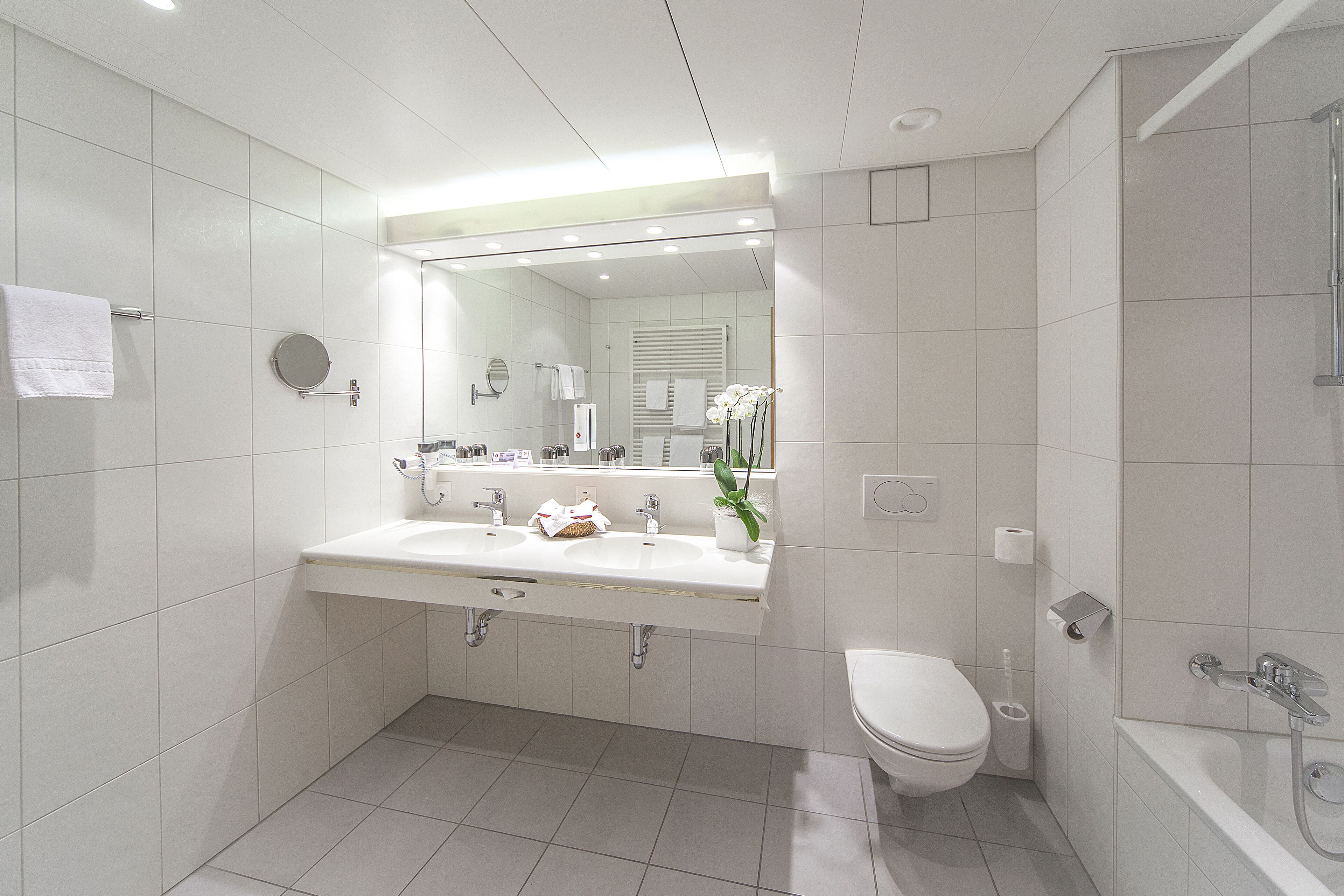 Un bagno moderno con lavandino, specchio, servizi igienici e vasca da bagno bianchi.