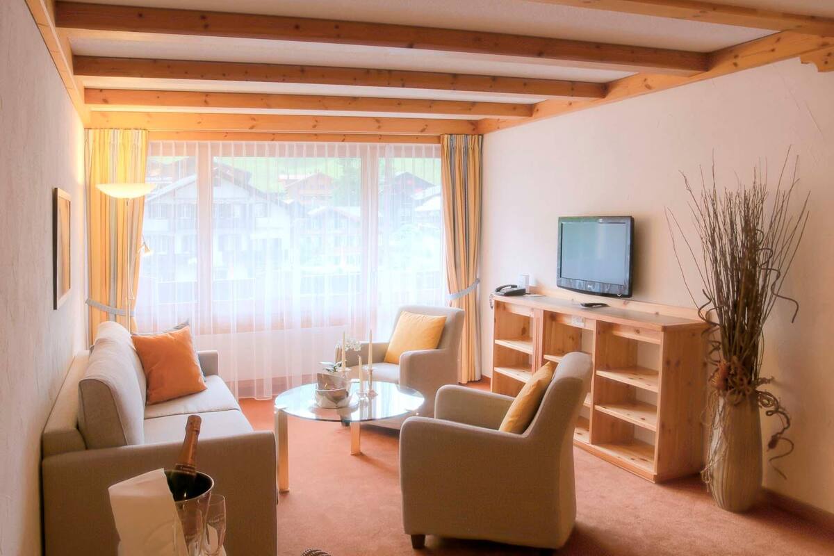 Un salon comprenant un canapé, deux fauteuils, une table basse, un téléviseur et une bibliothèque en bois.