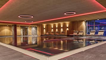 Una piscina interna moderna con rivestimenti in legno, illuminazione con luci rosse e poltrone relax.