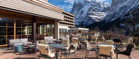 A patio with outdoor seating, a wooden building, and a mountain view.
